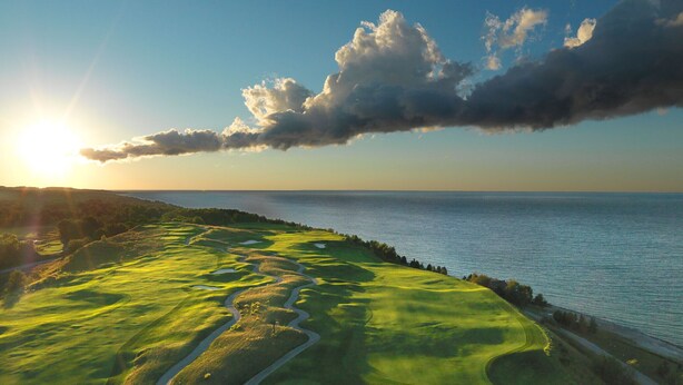 A coastal landscape with a golf course, a winding path, and a body of water. - Boyne Mountain on Resort Condo, close to Lifts, Lodge, Waterpark, all amenities (Boyne Falls)