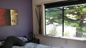 A bedroom with a bed, a window with a view of greenery, a wall art piece, and a nightstand with a lamp. - Entrance to the Lakes Getaway (Lakes Entrance)