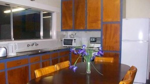 A kitchen with wooden cabinets, a round dining table with yellow chairs, a white refrigerator, and a microwave. - Entrance to the Lakes Getaway (Lakes Entrance)