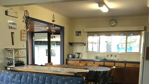 A compact living space with a sofa, dining table, and kitchen area including a refrigerator, sink, and window with curtains. - Entrance to the Lakes Getaway (Lakes Entrance)