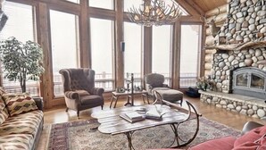 Ein geräumiges Wohnzimmer mit Kamin aus Stein, großen Fenstern und einer Kristallleuchter.