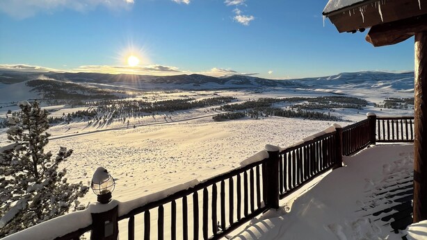 Ein mit Schnee bedeckter Balkon mit Blick auf eine verschneite Landschaft und einen klaren Himmel.