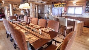 Ein rustikaler Essbereich aus Holz mit einem langen Tisch, gemusterten Untersetzern und einer Pendelleuchte.