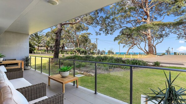 Ein Balkon mit Gartenmöbeln, Blick auf das Meer und umliegendes Grün.