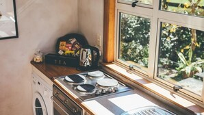 A compact kitchen with a stove, a washing machine, and a window with a view of greenery. - Lexington Park Cottage (Cambridge)