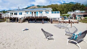 Un edificio frente a la playa con terraza, sillas de descanso y una zona de arena.