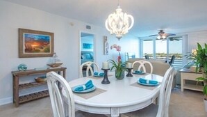 A dining area with a round table, chairs, a chandelier, a painting, and a view of the ocean. - Fully Renovated Waterfront Condo on Isla del Sol (St. Petersburg)