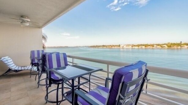 A balcony with striped chairs and a table, overlooking a calm body of water and a distant shoreline. - Fully Renovated Waterfront Condo on Isla del Sol (St. Petersburg)
