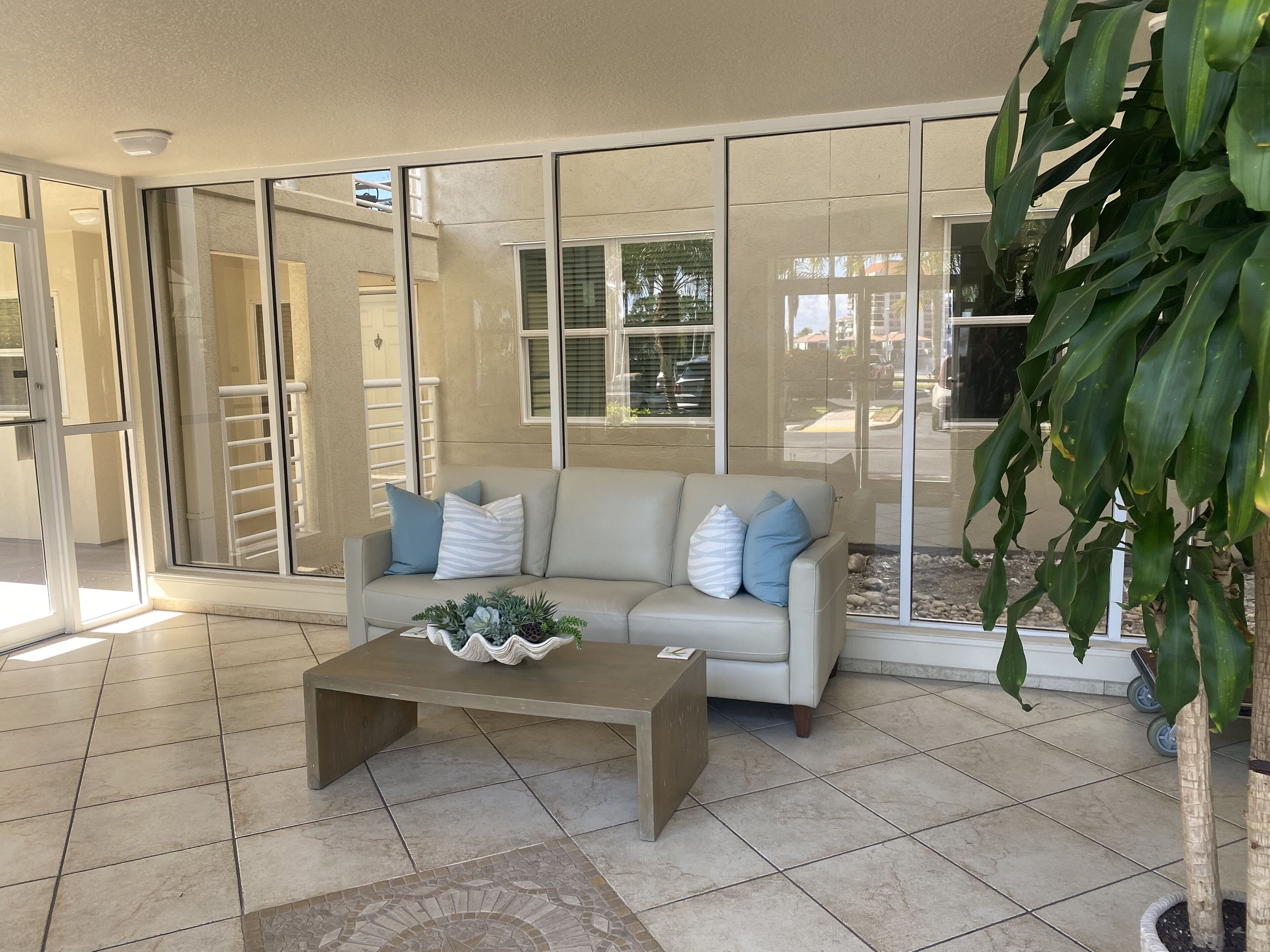 Un salón con un sofá color beige, una mesa de centro con plantas decorativas y puertas de cristal que dan a un área exterior.