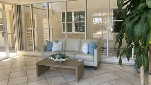 A living room with a beige sofa, a coffee table with decorative plants, and large glass doors leading to an outdoor area. - Fully Renovated Waterfront Condo on Isla del Sol (St. Petersburg)
