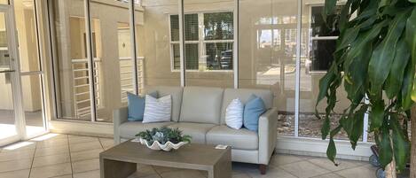 Un salón con un sofá color beige, una mesa de centro con plantas decorativas y puertas de cristal que dan a un área exterior.
