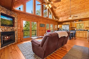 A cabin interior with a stone fireplace, a leather sofa, a dining area, and a kitchen. - Alpen Rose in Lansing, NC: Cozy 3-bedroom cabin retreat, perfect for 8! (Lansing)