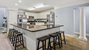 A modern kitchen with a central island, white cabinetry, stainless steel appliances, and a bar stool seating area. - Ocean Blvd Luxury Villas 205, Pool & Hot Tub (NORTH MYRTLE BEACH)