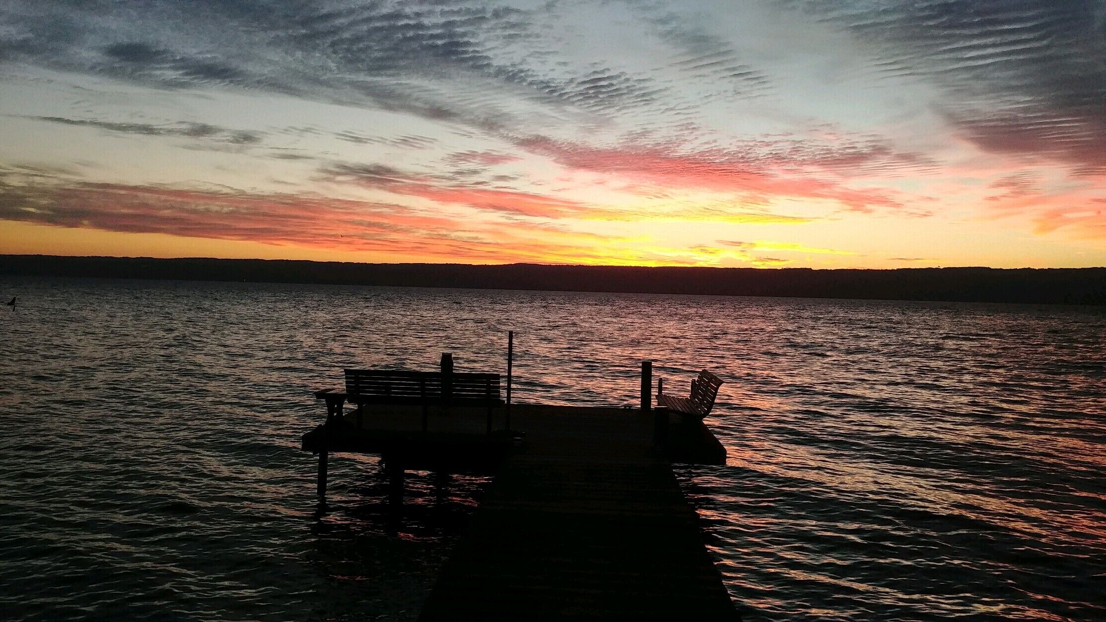 Une jetée s’avançant dans l’eau au coucher du soleil, avec un ciel dégagé au-dessus.