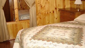 A cozy room with a wooden interior, a bed with a quilt, a bedside table with a lamp, and a framed picture on the wall. - Martins Vacation Rental (Hungry Horse)
