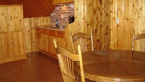 A wooden interior with a round dining table and chairs, a brick fireplace, and wooden cabinets. - Martins Vacation Rental (Hungry Horse)