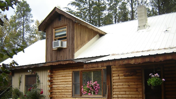 A rustic log cabin with a metal roof, a front porch, and a window with pink flowers. - Martins Vacation Rental (Hungry Horse)
