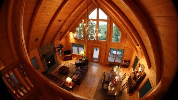 A cozy, wooden interior with a vaulted ceiling, a fireplace, a dining area, and large windows offering a view of the outdoors.