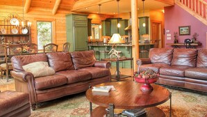 A spacious living room with leather sofas, a wooden coffee table, and a dining area with green cabinets and pendant lights.
