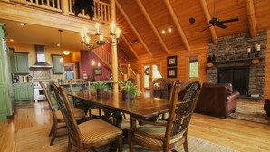 A spacious dining area with a wooden table and chairs, a staircase leading to an upper level, and a stone fireplace.
