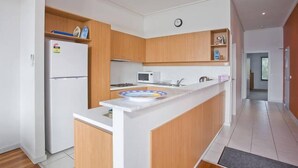 A modern kitchen with wooden cabinets, a white refrigerator, a microwave, and a sink. - Lorne Penthouse - water views (Lorne)
