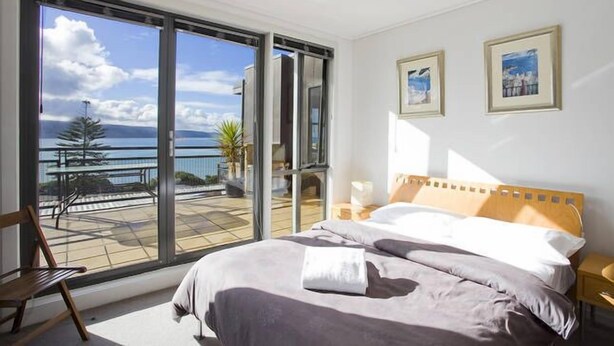A bedroom with a large sliding glass door leading to a balcony with a view of the sea. - Lorne Penthouse - water views (Lorne)