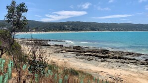 A coastal landscape with a sandy beach, rocky shoreline, and a distant view of a forested hill. - Lorne Penthouse - water views (Lorne)