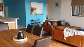 A modern living room with a wooden dining table, leather sofa, and a blue accent wall. - Lorne Penthouse - water views (Lorne)