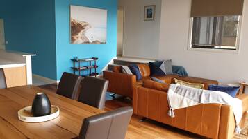 A modern living room with a wooden dining table, leather sofa, and a blue accent wall.
