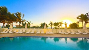 A poolside area with lounge chairs and umbrellas, palm trees, and a sunset view. - Private Beachfront Condominium with Breathtaking Views and Resort Access (Sunny Isles Beach)