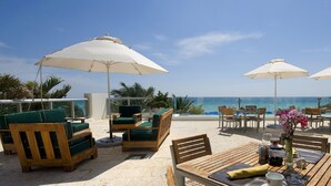 A beachside patio with wooden furniture, white umbrellas, and a view of the ocean. - Private Beachfront Condominium with Breathtaking Views and Resort Access (Sunny Isles Beach)