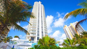 A tall, modern hotel with a curved facade, surrounded by palm trees and a clear blue sky. - Private Beachfront Condominium with Breathtaking Views and Resort Access (Sunny Isles Beach)