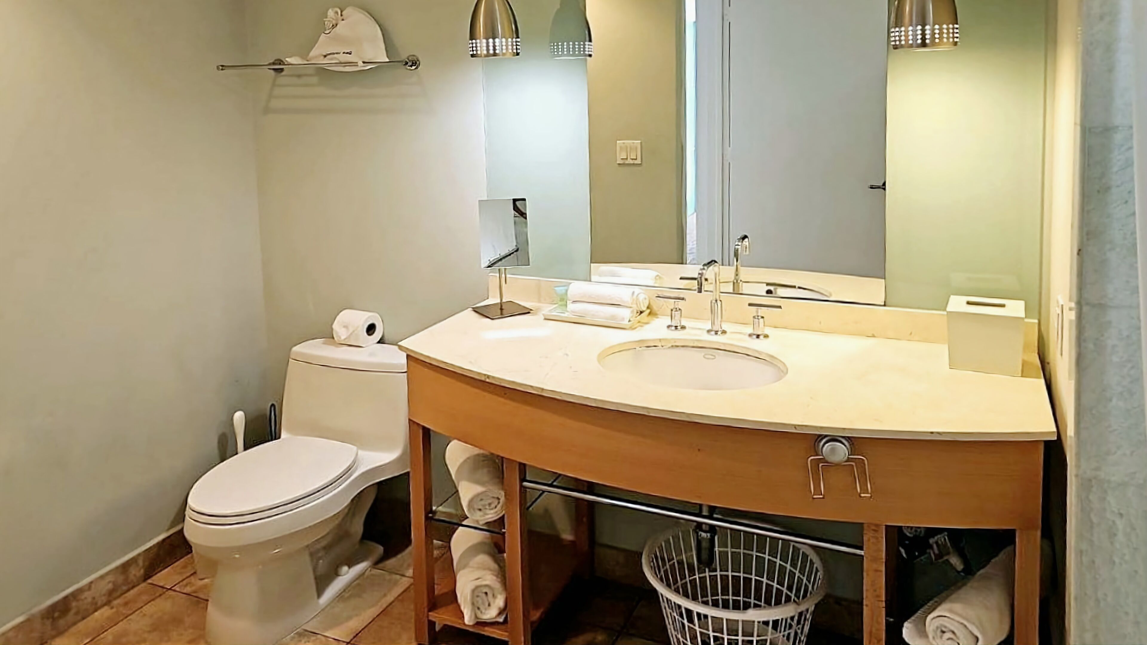 Une salle de bain équipée d’un WC, d’un lavabo, d’un miroir, d’un porte-serviettes et d’une poubelle.