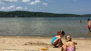 Une plage bordée d’un lac, des personnes dans l’eau et, au loin, une colline couverte de forêt.