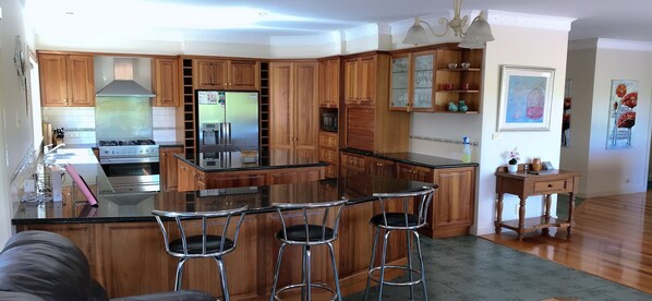 Une cuisine moderne avec des meubles en bois, un réfrigérateur en acier inoxydable, une cuisinière à gaz et un coin bar avec des tabourets.