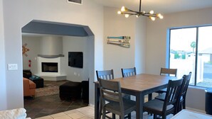 A dining area with a wooden table and chairs, a fireplace, and a view through a large window.