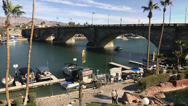 A bridge over a river with boats docked at the marina, palm trees, and a sign indicating the marina is open.