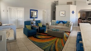A living room with a beige sofa, blue armchairs, a coffee table, and a colorful rug.