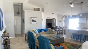 A modern living room with a sofa set, a dining area, and a kitchen.