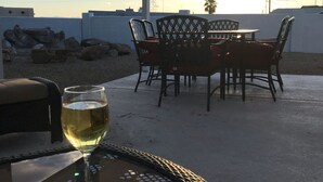 An outdoor patio with a table and chairs, a glass of white wine, and a view of the sunset.