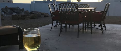 Eine Terrasse im Freien mit Tisch und Stühlen, einem Glas Weißwein und Blick auf den Sonnenuntergang.