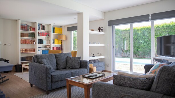 A modern living room with a grey sofa, a wooden coffee table, and a bookshelf filled with books. - Lovely House in Lisbon coast For 8 guests (São Domingos de Rana)