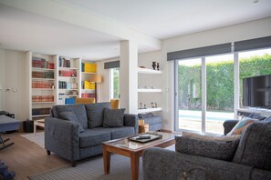 A modern living room with a grey sofa, a wooden coffee table, and a bookshelf filled with books. - Lovely House in Lisbon coast For 8 guests (São Domingos de Rana)