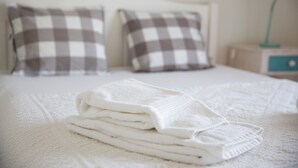 A neatly made bed with a white blanket and pillows, a bedside table with a lamp, and a nightstand with a drawer. - Lovely House in Lisbon coast For 8 guests (São Domingos de Rana)