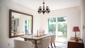 A dining area with a wooden table, white chairs, a chandelier, and a large mirror on the wall. - Lovely House in Lisbon coast For 8 guests (São Domingos de Rana)