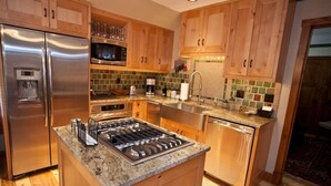 Una cocina moderna con armarios de madera, electrodomésticos de acero inoxidable, encimera de granito y salpicadero de azulejos.