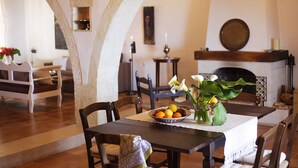 Uma área de refeições com uma mesa posta para dois, um vaso com flores e uma fruteira.