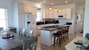 A modern kitchen with white cabinets, a central island with bar stools, a built-in microwave, and a coffee maker.