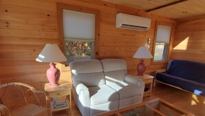 Ein Holzblockhaus-Interieur mit einer Couch, einem Sessel und einem Couchtisch mit Glastischplatte.