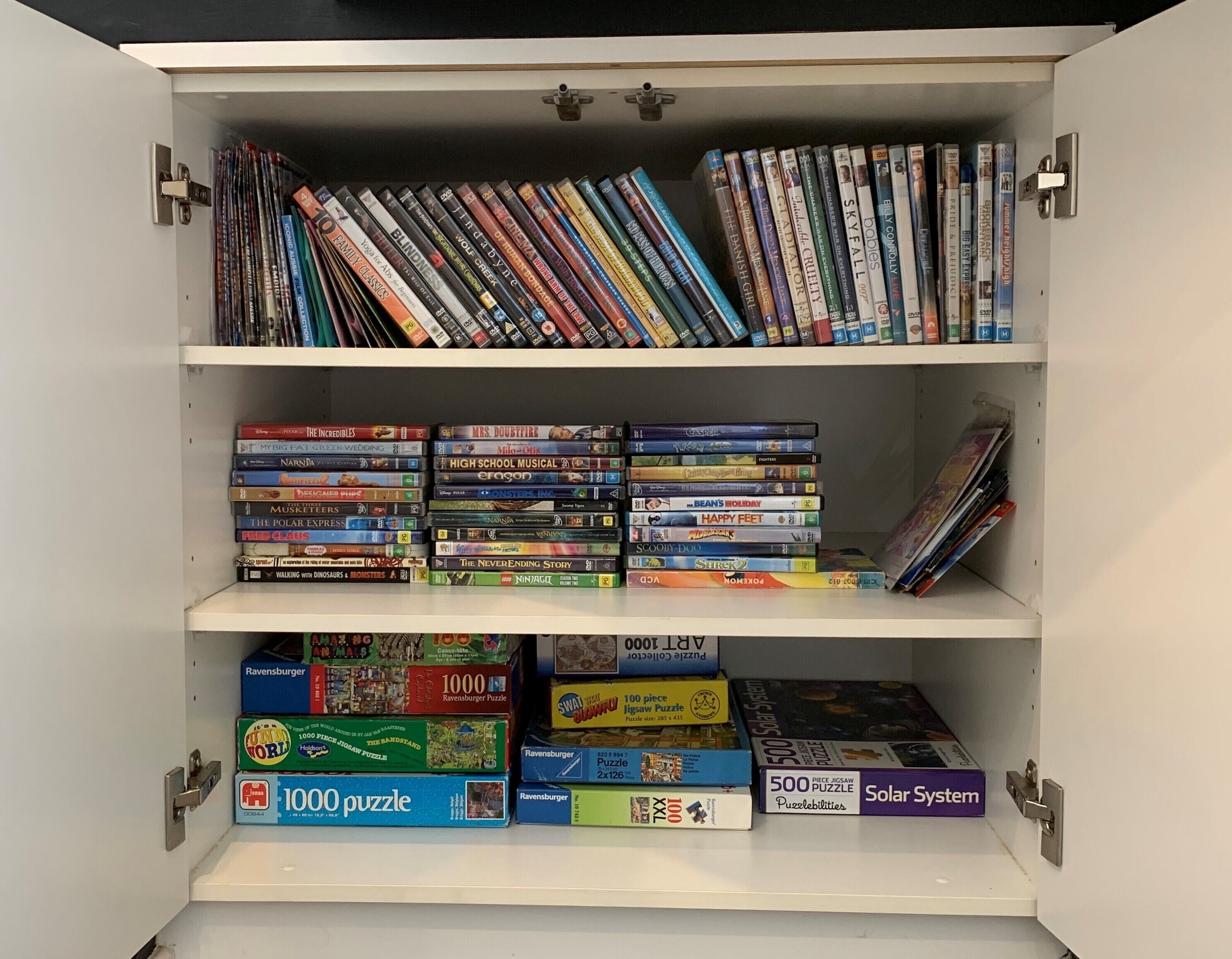 A bookshelf with various books and DVDs, including puzzle books and a solar system book.